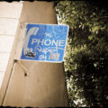 Old telephone sign with stickers and graffiti all over it