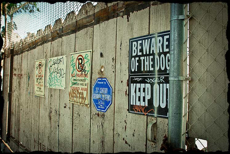 Wooden gate of a business with signs, which have all been graffitied.