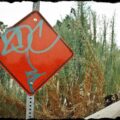 Graffiti spray painted on red diamond sign near freeway.