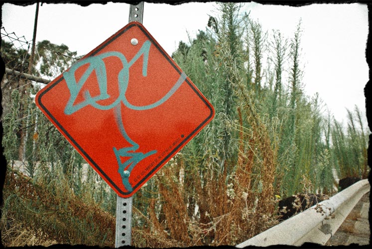 Graffiti spray painted on red diamond sign near freeway.
