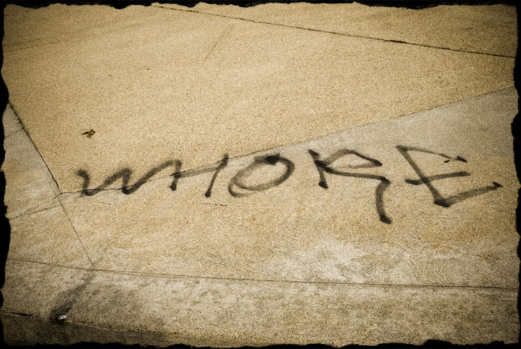 The word "whore" spray painted on the corner of the sidewalk