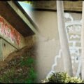 On the side of freeway overpass, graffiti of a robot and the word "botz"