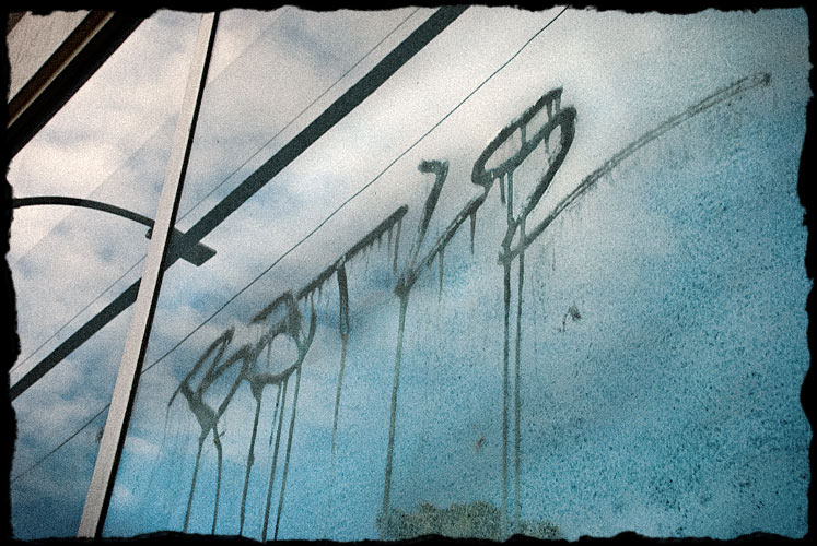 Graffiti spray painted on window of a business. Looks like 
