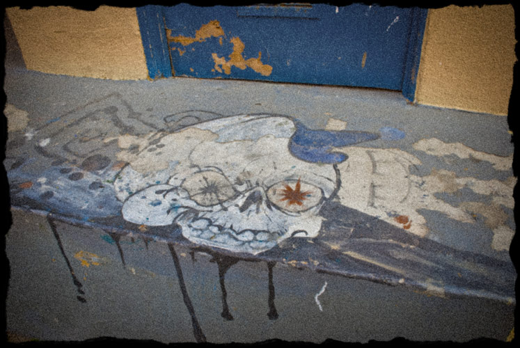 Graphic of skull wearing a hat on the cement porch behind a business.